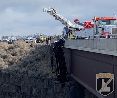 A Ford F-350 hangs by a trailer safety chain from an I-85 bridge over Malad Gorge in Idaho as rescuers scramble to save the couple and their dogs inside.