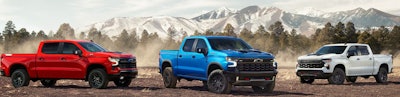 red blu white 2024 Chevy Silverado pickup trucks lined up mountain background